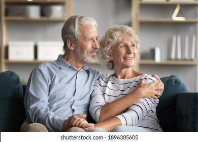 Dreamy middle aged senior loving retired family couple looking in distance, planning common future or recollecting memories, enjoying peaceful moment relaxing together on cozy sofa in living room. - Shutterstock ID 1896305605