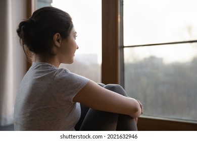 Dreamy millennial Indian woman look in window distance thinking or making plans of perspectives opportunities. Pensive young ethnic female dreaming or visualizing at home. Vision concept.