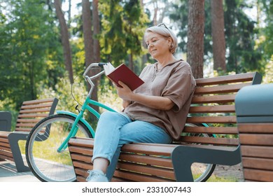 Dreamy modern old lady relaxing city park. Pensive senior gray haired woman casual sitting wooden bench outdoors reading book. cycling forest park, bicycle, healthy active lifestyle after 50-60 years - Shutterstock ID 2331007443