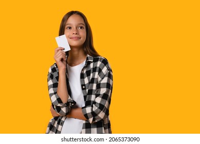 Dreamy pensive thoughtful caucasian teenager girl pupil student dreaming about winning a lot of money, lottery, online shopping, new clothes, presents holding credit card isolated in yellow background