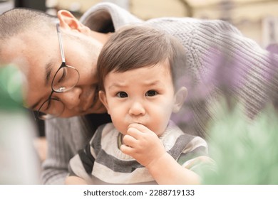 Dreamy picture of male infant staring looking at camera sitting on his father's legs with glasses in beer garden at the pub in Scotland, Edinburgh. Bokeh with plant. Multicultural family, mixed race. - Powered by Shutterstock