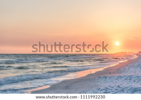 Dreamy pink peach orange sunset in Santa Rosa Beach, Florida with Pensacola coastline coast cityscape skyline in panhandle with ocean gulf mexico waves, birds