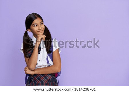 Dreamy smiling indian preteen girl, latin kid schoolgirl wears uniform and backpack looking away at copy space, dreaming, thinking, choosing, advertising standing isolated on lilac violet background.