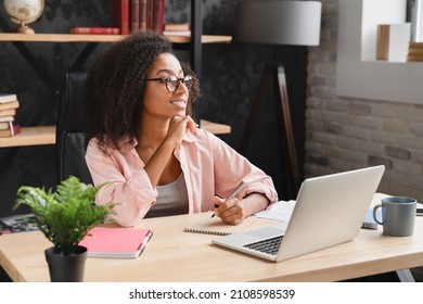 Dreamy Thoughtful Young African Tutor Student Schoolgirl Writing Essay, Poem, Novel With Imagination, Doing Homework Assignment Using Laptop At Office Desk