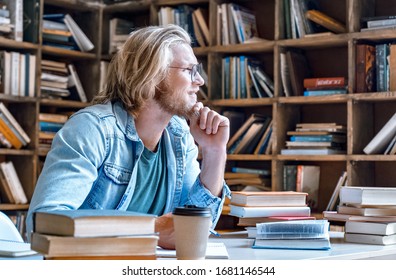 Dreamy thoughtful young teacher man male student hipster author glasses chin on hand study in library sit at desk write essay ready for exam do homework assignment smile look away education concept.