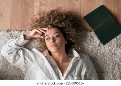 Dreamy woman with book lying on floor - Shutterstock ID 2208895167