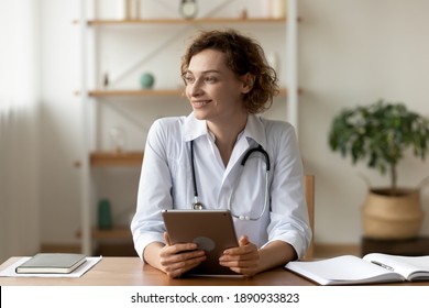 Dreamy young 35s general practitioner doctor holding digital tablet in hands, looking in distance. Happy female doc physician thinking of career opportunities or visualizing professional future.