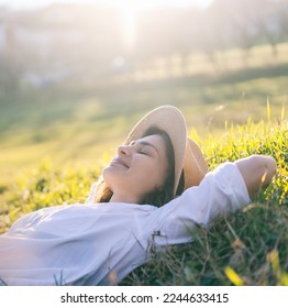 Dreamy young beautiful woman in hat lying on green grass with closed eyes enjoying summer sun and spring day - Powered by Shutterstock