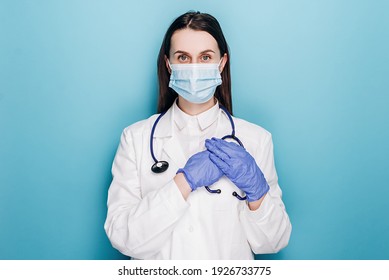 Dreamy Young Female Nurse Or Doctor In Protective Face Mask And Latex Gloves, Press Hands To Heart, Daydreaming, Keep In Mind, Isolated On Blue Background. Medical Workers, Covid-19 Pandemic Concept