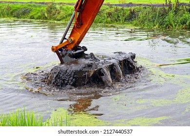 Dredging, crane with backhoe takes a scoop of sediment from a canal