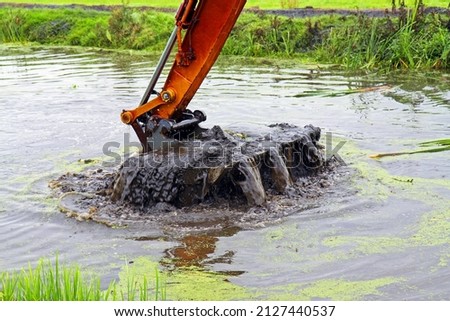 Dredging, crane with backhoe takes a scoop of sediment from a canal