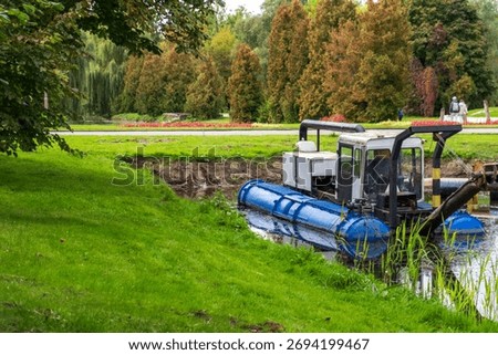 A dredging machine on a small river in a park setting.