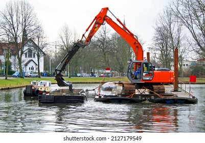 Dredging of urban canals by crane from a pontoon, the dredging spoil is deposited in a barge for transportation  Leiden, Netherlands