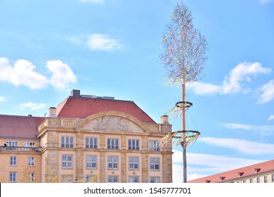 Dresden, Germany - May 2019. Maypole With Colorful Ribbons On Blue Sky Background.  Traditional Spring Holiday In Germany. May Pole With A Beautiful Wreath Decorated Bright Holiday Ribbons