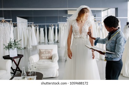 Dress Designer Fitting Bridal Gown To Woman In Boutique. Women Checking And Making Adjustment To Wedding Gown In Professional Fashion Designer Studio.