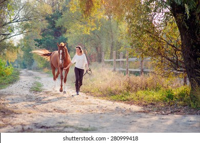 Dressage. Beautiful young woman running with her brown horse at countryside.