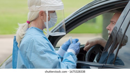 Dressed in full protective gear healthcare worker collects sample from mature man sitting inside his car as part the operations coronavirus mobile testing unit 