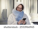 Dressed in warm layers, a girl happily checks her phone while shopping for Christmas gifts outdoors.