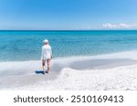 Dressed in white, she stands at the edge of the tranquil sea, gazing into the infinite horizon where the blue ocean meets the sky.