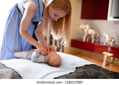 The dressing of baby boy on a bed. Mother or nanny dresses newborn child in blue clothes