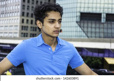 Dressing in blue T shirt and standing in the front of a business district, a young asian teenager is thoughtfully looking forward./City Boy