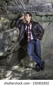 Dressing in a dark brown leather jacket, a long red pattern scarf, a handsome middle age guy is standing by rocks, relaxing and thinking. / Relaxing and Thinking 