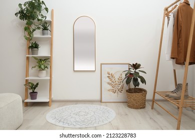 Dressing room interior with wooden furniture, mirror and houseplants near white wall. Stylish accessories