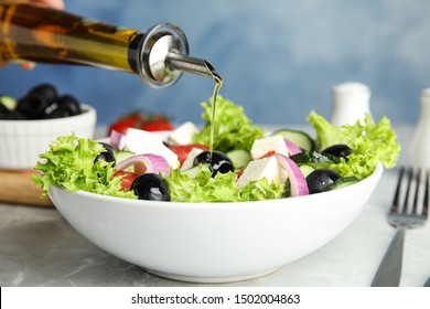 Dressing Tasty Fresh Greek Salad With Olive Oil On Grey Marble Table