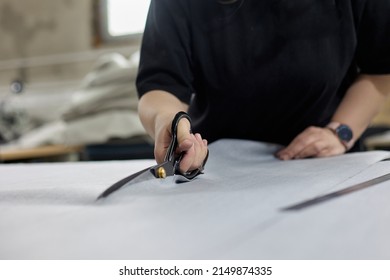 Dressmaker In A Smart Watch Cuts A Piece Of Fabric With Scissors In A Sewing Workshop. Production Of Piece Of Modern Clothing Or Upholstery For Upholstered Furniture Made Of Fabric In Studio Workshop