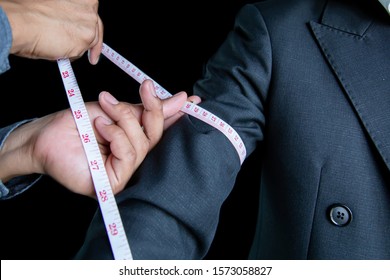The dressmaker was using a tape measure to measure the length of the arm on a black background.