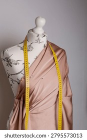 Dressmaking process on a mannequin using draping technique. Beige fabric is pinned with sewing pins to create a garment design in a fashion atelier.