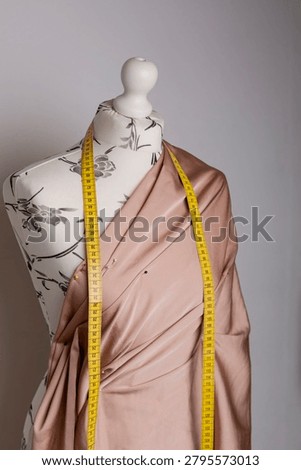 Dressmaking process on a mannequin using draping technique. Beige fabric is pinned with sewing pins to create a garment design in a fashion atelier.