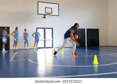 Dribbling basketball around cones, coach training female basketball team in gym, copy space. teamwork, gymnasium, sports, practice, female athletes, exercise - Powered by Shutterstock