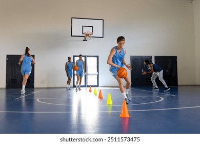 Dribbling basketball around cones, female athlete training in school gym, copy space. Sports, exercise, practice, fitness, determination, agility - Powered by Shutterstock