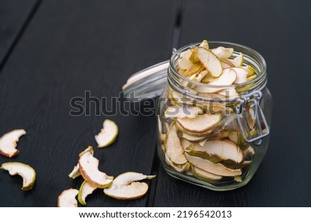 Dried apple slices in open glass jar. Homemade organic dried apple chips with fresh apple on black table background. Sweet vegan snack. Healthy and nutrition concept. Shallow depth of field