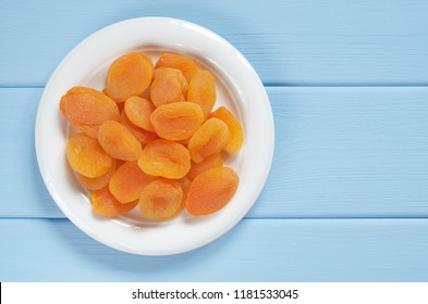 Dried apricots in plate on blue wooden table, top view with copy space