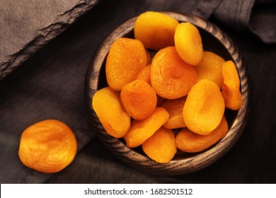 Dried apricots in a wooden plate on a dark background. Dry fruits on the kitchen table in retro style. View from above
