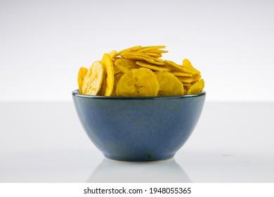 Dried banana chips or banana waffers,arranged beautifully in a aqua rustic  ceramic bowl with white textured background.