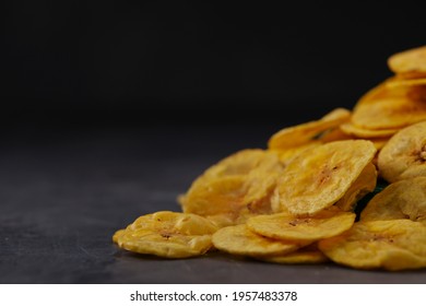 Dried banana chips or banana waffers,scattered over a green round base with grey textured background, isolated.
