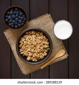 Dried Berry And Oatmeal Breakfast Cereal In Rustic Bowl With Glass Of Milk And Fresh Blueberries, Photographed Overhead On Dark Wood With Natural Light 