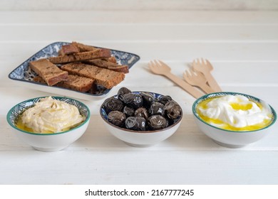 Dried Black Olives, Yogurt With Olive Oil, Tahini Paste For Mediterranean Breakfast On White Wooden Background.