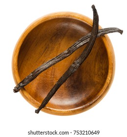 Dried Bourbon vanilla pods over empty wooden bowl. Two dark brown ripe fruits of Vanilla planifolia. 
Spice with distinctive flavor, used in baking. Macro food photo close up from above over white.