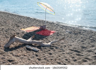 A Dried Branch Next To An Umbrella And Two Beach Towels On The Sand In San Vincenzo, Italy. High Quality Photo