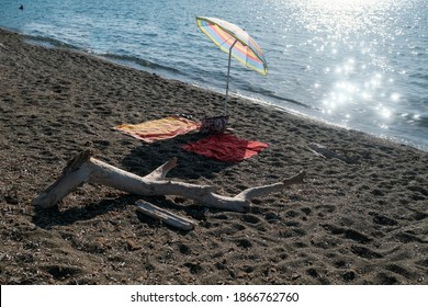 A Dried Branch Next To An Umbrella And Two Beach Towels On The Sand In San Vincenzo, Italy. High Quality Photo