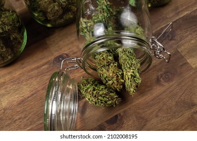 Dried Cannabis Hemp Buds Spill Out Of A Glass Jar, Ready For Consumption.