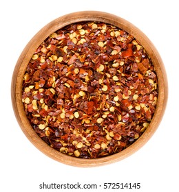 Dried Chili Pepper Flakes In Wooden Bowl. Dried And Crushed Fruits Of Capsicum Frutescens, Used As Hot Spice And For Tabasco Sauce. Isolated Macro Food Photo Close Up From Above On White Background.