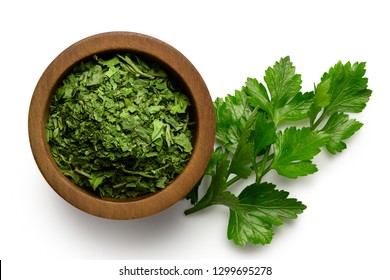 Dried Chopped Parsley In Dark Wood Bowl Next To Fresh Parsley Leaves Isolated On White From Above.