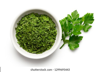 Dried Chopped Parsley In White Ceramic Bowl Next To Fresh Parsley Leaves Isolated On White From Above.