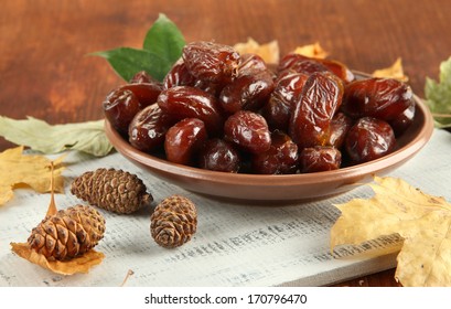 Dried dates on plate with yellow leaves on wooden background