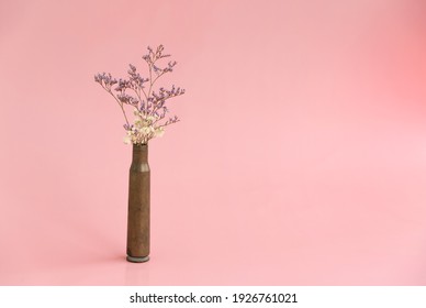 Dried flowers in an empty case from under a firearm on a pink background